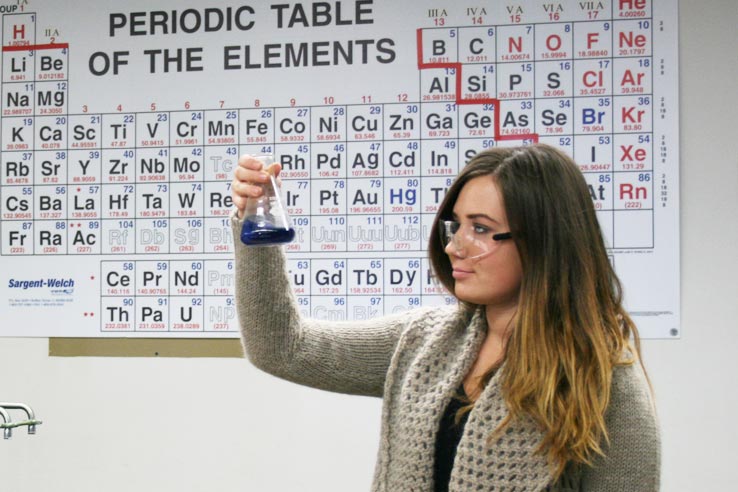 A student looking at a beaker with chemicals in it.